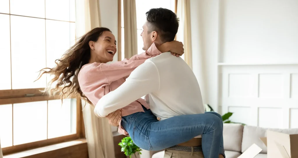 Pareja joven celebrando con alegría su mudanza a un nuevo hogar luminoso en Nueva Valdeluz mientras el hombre levanta a la mujer.