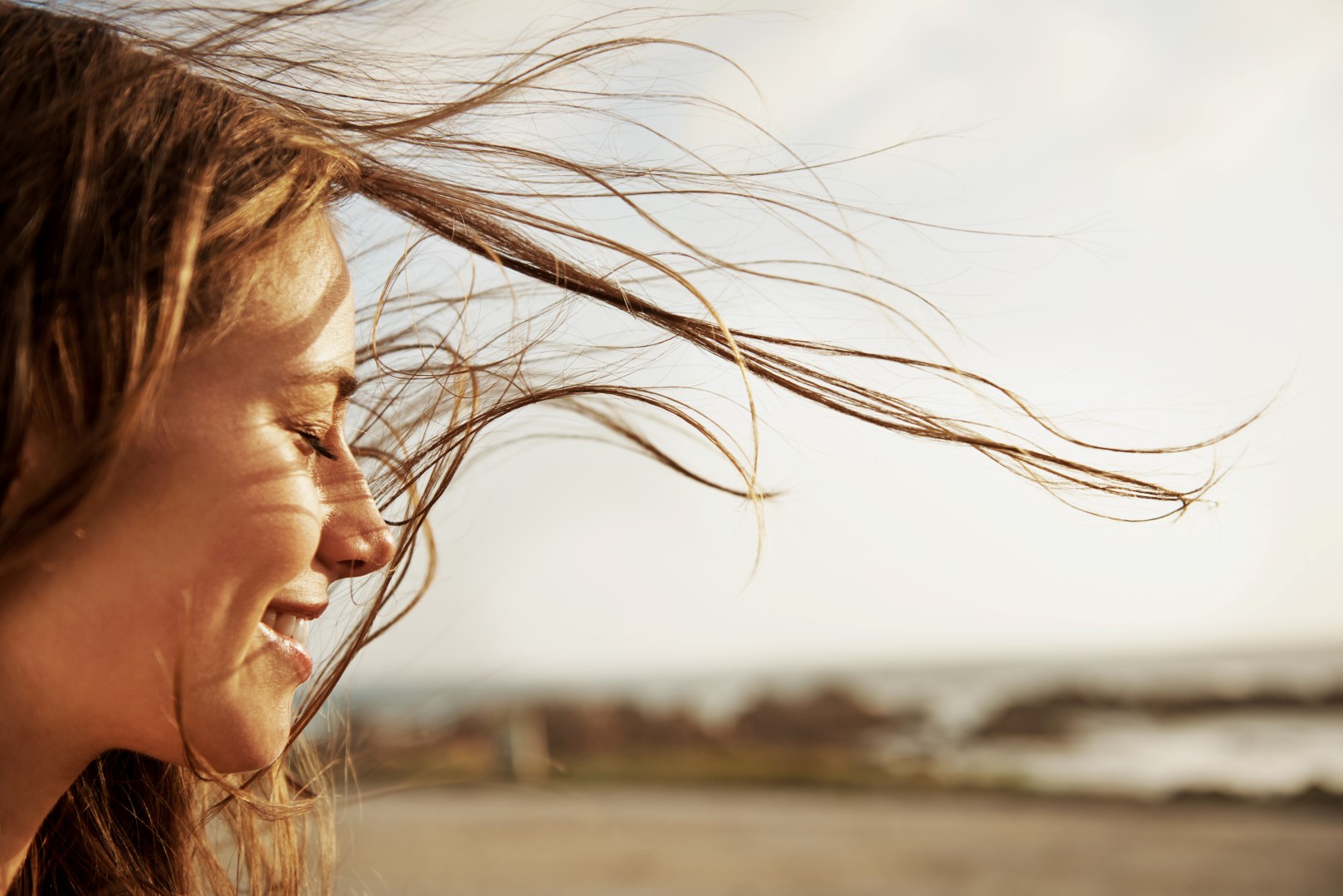 Primer plano de perfil de una mujer sonriendo con los ojos cerrados y el cabello al viento en un entorno natural al aire libre en Valdeluz